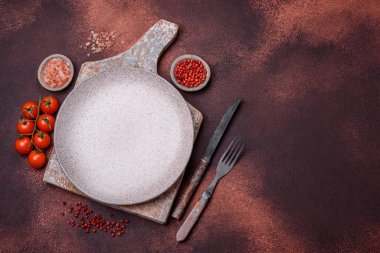 Empty ceramic round plate on dark textured concrete background. Cutlery, preparation for dinner