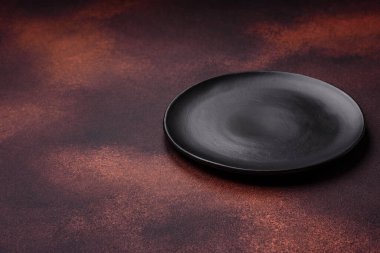 Empty ceramic round plate on dark textured concrete background. Cutlery, preparation for dinner
