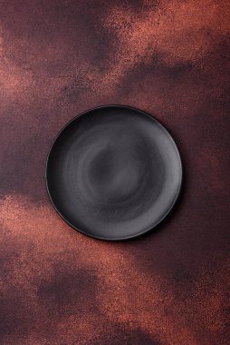 Empty ceramic round plate on dark textured concrete background. Cutlery, preparation for dinner