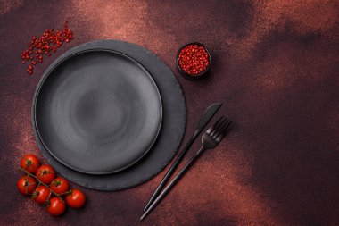 Empty ceramic round plate on dark textured concrete background. Cutlery, preparation for dinner