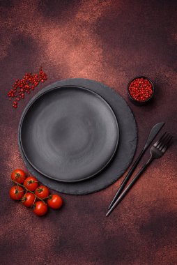 Empty ceramic round plate on dark textured concrete background. Cutlery, preparation for dinner