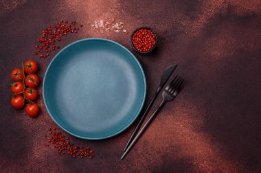 Empty ceramic round plate on dark textured concrete background. Cutlery, preparation for dinner