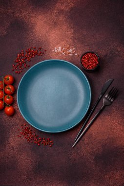 Empty ceramic round plate on dark textured concrete background. Cutlery, preparation for dinner