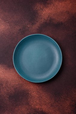 Empty ceramic round plate on dark textured concrete background. Cutlery, preparation for dinner