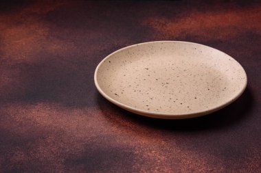 Empty ceramic round plate on dark textured concrete background. Cutlery, preparation for dinner