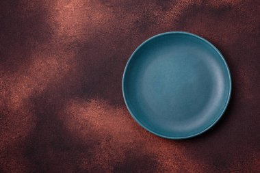 Empty ceramic round plate on dark textured concrete background. Cutlery, preparation for dinner