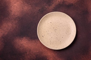 Empty ceramic round plate on dark textured concrete background. Cutlery, preparation for dinner