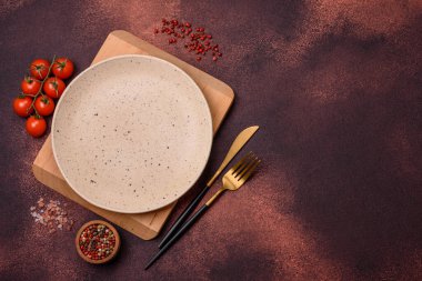Empty ceramic round plate on dark textured concrete background. Cutlery, preparation for dinner