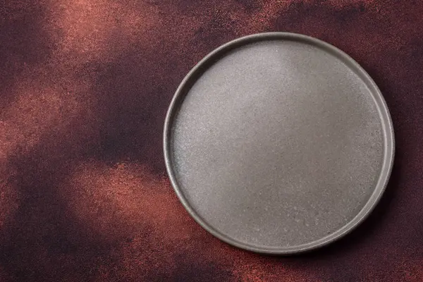 Empty ceramic round plate on dark textured concrete background. Cutlery, preparation for dinner