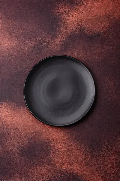 Empty ceramic round plate on dark textured concrete background. Cutlery, preparation for dinner