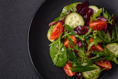 Lezzetli taze salata roka, ıspanak, salatalık ve kiraz domatesli koyu beton kaplama seramik bir tabakta.