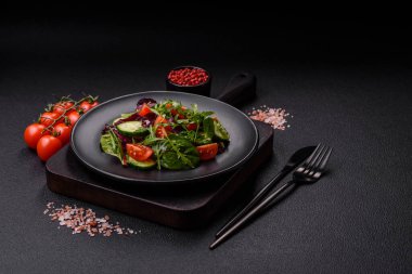 Lezzetli taze salata roka, ıspanak, salatalık ve kiraz domatesli koyu beton kaplama seramik bir tabakta.