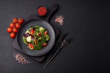 Lezzetli taze salata roka, ıspanak, salatalık ve kiraz domatesli koyu beton kaplama seramik bir tabakta.