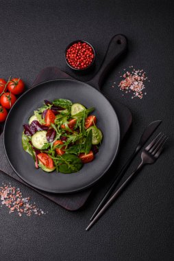 Lezzetli taze salata roka, ıspanak, salatalık ve kiraz domatesli koyu beton kaplama seramik bir tabakta.