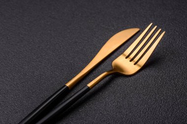 Çatal bıçak, bıçak ve kaşık koyu dokulu beton arka planda. Mutfak eşyaları ve aksesuarları.