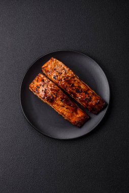 Sos ve susamlı lezzetli kırmızı somon balığı, koyu beton arka planda baharatlar ve otlar.