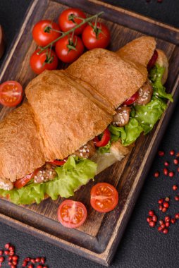 Lezzetli taze kruvasan, tavuk ya da sığır eti, marul, domates, baharat ve koyu beton arka planda sos.