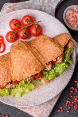 Lezzetli taze kruvasan, tavuk ya da sığır eti, marul, domates, baharat ve koyu beton arka planda sos.