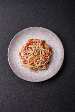 Lezzetli pirinç eriştesi veya koyu beton bir arka planda tavuk, havuç, biber, tuz, baharat ve otlarla udon.