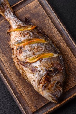 Izgarada pişirilmiş leziz dorado. Koyu dokulu arka planda tuz, baharat ve otlarla.