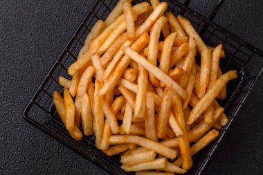 Koyu beton bir arka planda tuzlu ve baharatlı lezzetli çıtır altın kızartmalar.