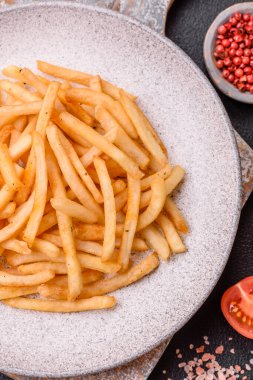 Koyu beton bir arka planda tuzlu ve baharatlı lezzetli çıtır altın kızartmalar.