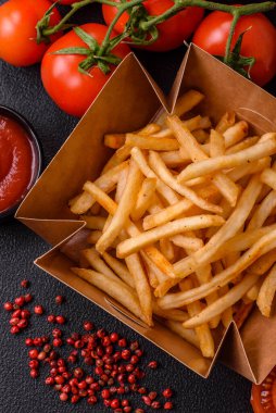 Koyu beton bir arka planda tuzlu ve baharatlı lezzetli çıtır altın kızartmalar.