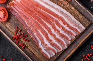 Baharat ve otlarla dilimlenmiş taze çiğ domuz pastırması ve koyu beton bir arka plan.