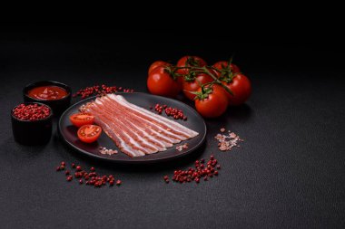 Baharat ve otlarla dilimlenmiş taze çiğ domuz pastırması ve koyu beton bir arka plan.