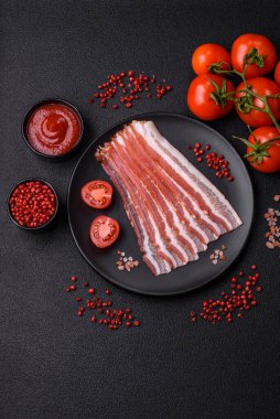 Baharat ve otlarla dilimlenmiş taze çiğ domuz pastırması ve koyu beton bir arka plan.