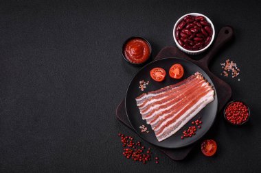 Baharat ve otlarla dilimlenmiş taze çiğ domuz pastırması ve koyu beton bir arka plan.