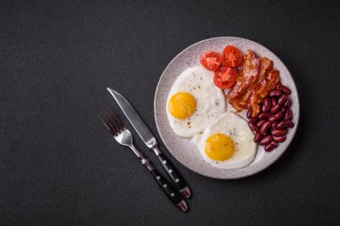 Yağda yumurta, pastırma, fasulye, domates, baharat ve bitkilerle İngiliz kahvaltısı. Güne doyurucu ve doyurucu bir başlangıç.