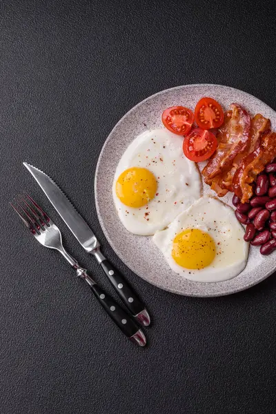English breakfast with fried eggs, bacon, beans, tomatoes, spices and herbs. A hearty and nutritious start of the day