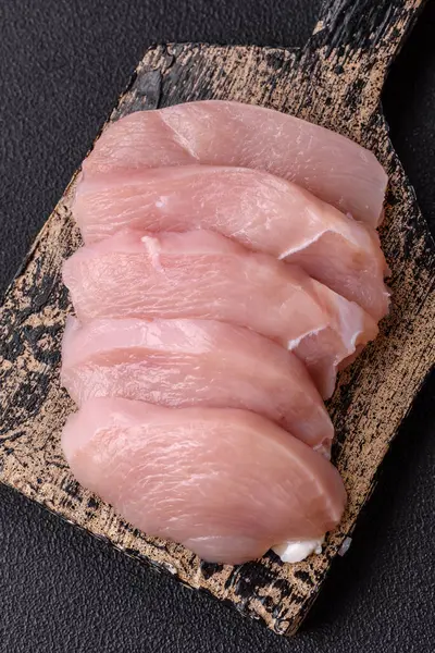 Slices of raw chicken or turkey fillet with salt, spices and herbs on a dark concrete background