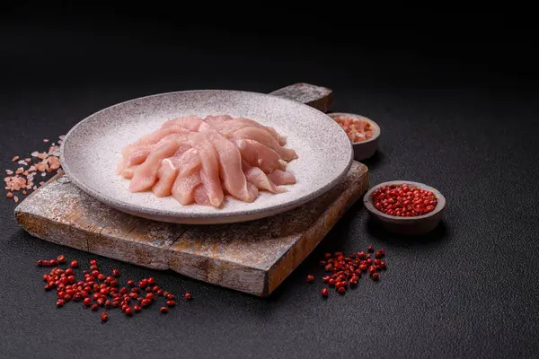 Slices of raw chicken or turkey fillet with salt, spices and herbs on a dark concrete background
