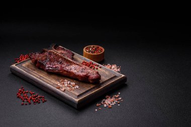 Lezzetli biftek, tuz, baharat ve otlarla birlikte koyu beton bir arka planda.