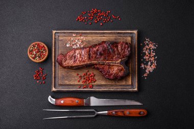 Lezzetli biftek, tuz, baharat ve otlarla birlikte koyu beton bir arka planda.