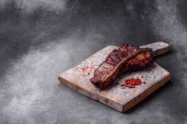 Lezzetli biftek, tuz, baharat ve otlarla birlikte koyu beton bir arka planda.