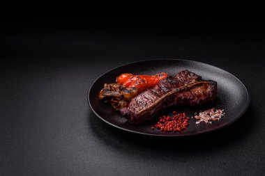 Lezzetli biftek, tuz, baharat ve otlarla birlikte koyu beton bir arka planda.