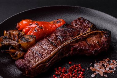 Lezzetli biftek, tuz, baharat ve otlarla birlikte koyu beton bir arka planda.