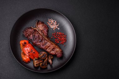 Lezzetli biftek, tuz, baharat ve otlarla birlikte koyu beton bir arka planda.