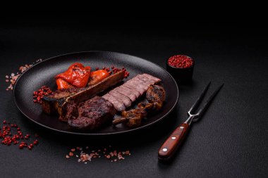 Lezzetli biftek, tuz, baharat ve otlarla birlikte koyu beton bir arka planda.