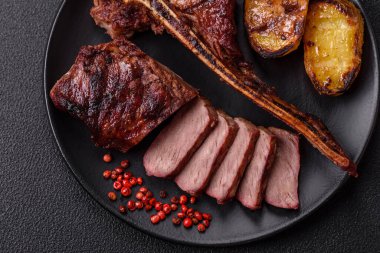 Lezzetli biftek, tuz, baharat ve otlarla birlikte koyu beton bir arka planda.