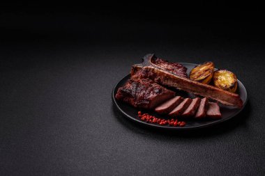 Lezzetli biftek, tuz, baharat ve otlarla birlikte koyu beton bir arka planda.