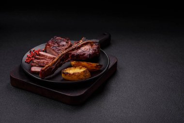 Lezzetli biftek, tuz, baharat ve otlarla birlikte koyu beton bir arka planda.