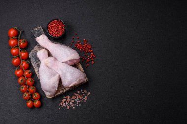 Taze çiğ tavuk bacağı, koyu beton arka planda tuz ve baharatlar.