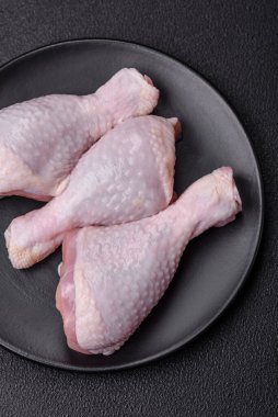 Taze çiğ tavuk bacağı, koyu beton arka planda tuz ve baharatlar.