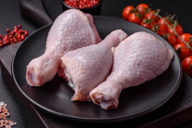 Taze çiğ tavuk bacağı, koyu beton arka planda tuz ve baharatlar.