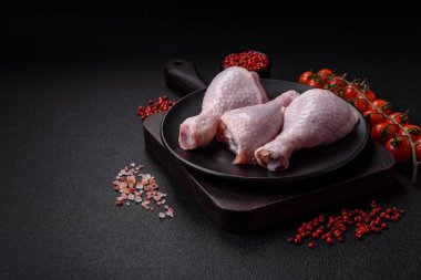 Taze çiğ tavuk bacağı, koyu beton arka planda tuz ve baharatlar.