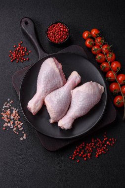 Taze çiğ tavuk bacağı, koyu beton arka planda tuz ve baharatlar.